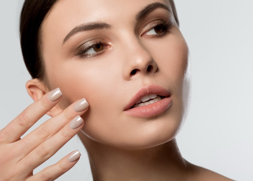 Close up of female pretty face. Peaceful young lady touching her cheek while applying moisturizer. Isolated
