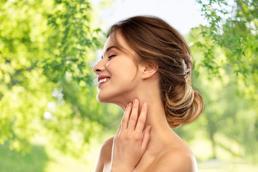 beauty and people concept - smiling young woman touching her neck over green natural background