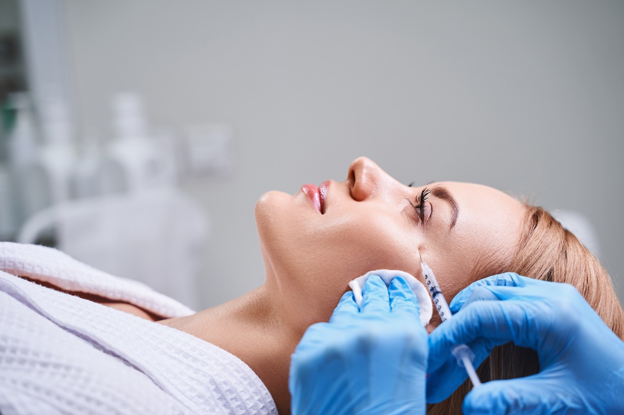 Young woman is visiting cosmetologist and lying on couch while professional is giving her face antiage fillers